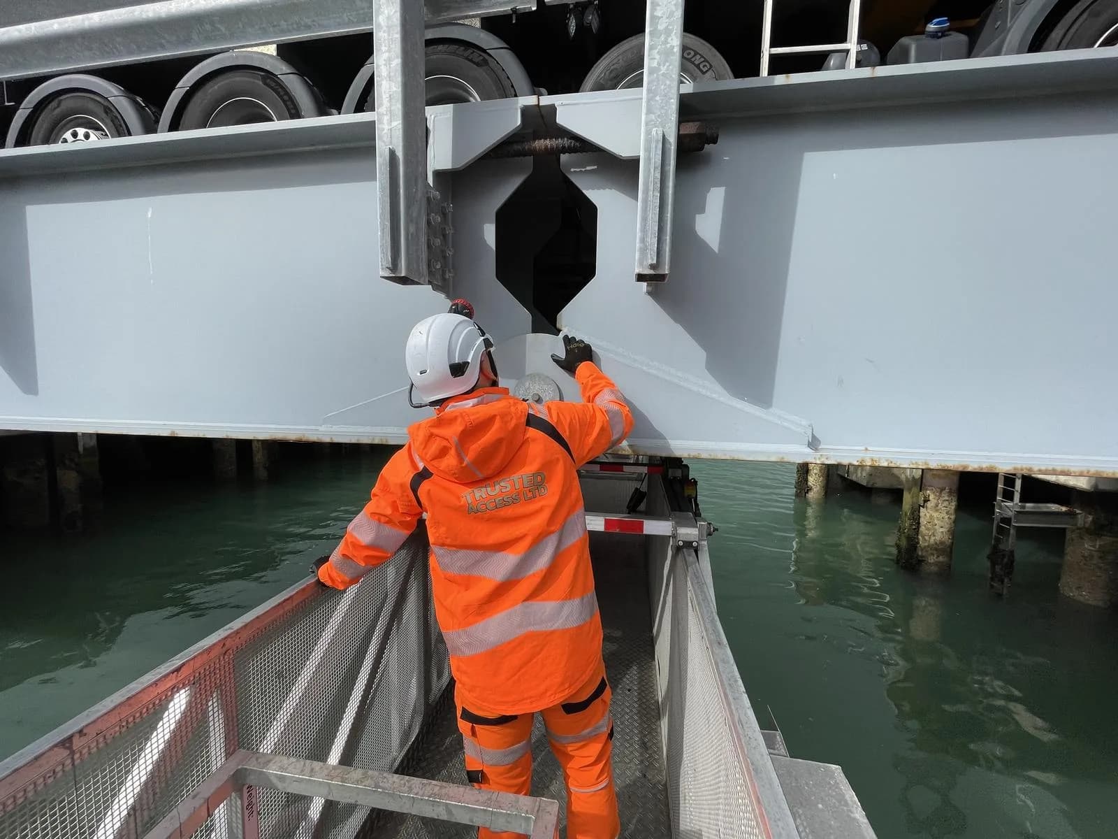 Inspector in Trusted Access hi-vis examining a bridge bearing beneath the deck