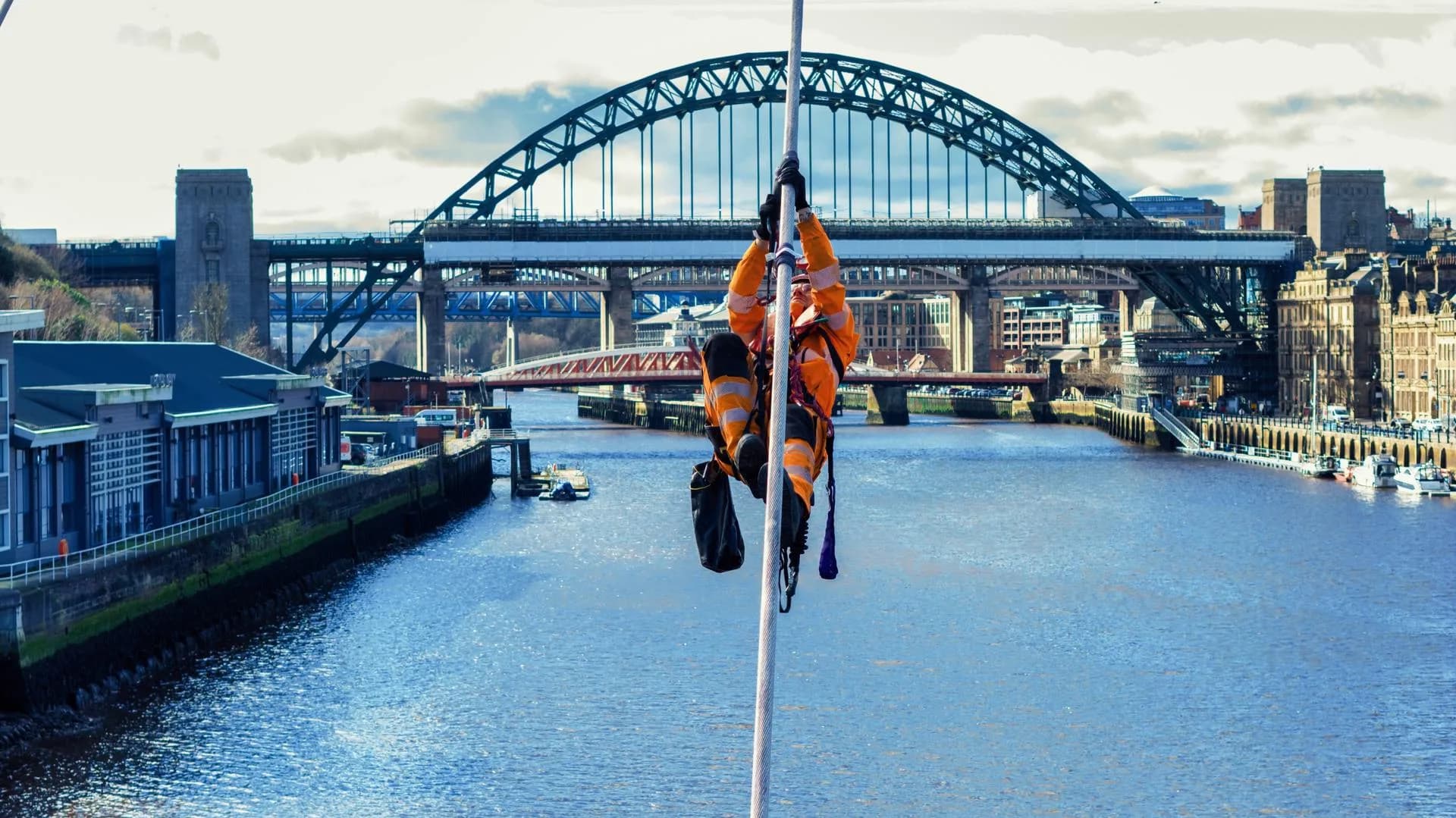 Rope access technician descending a line above the River Tyne with the Tyne Bridge behind