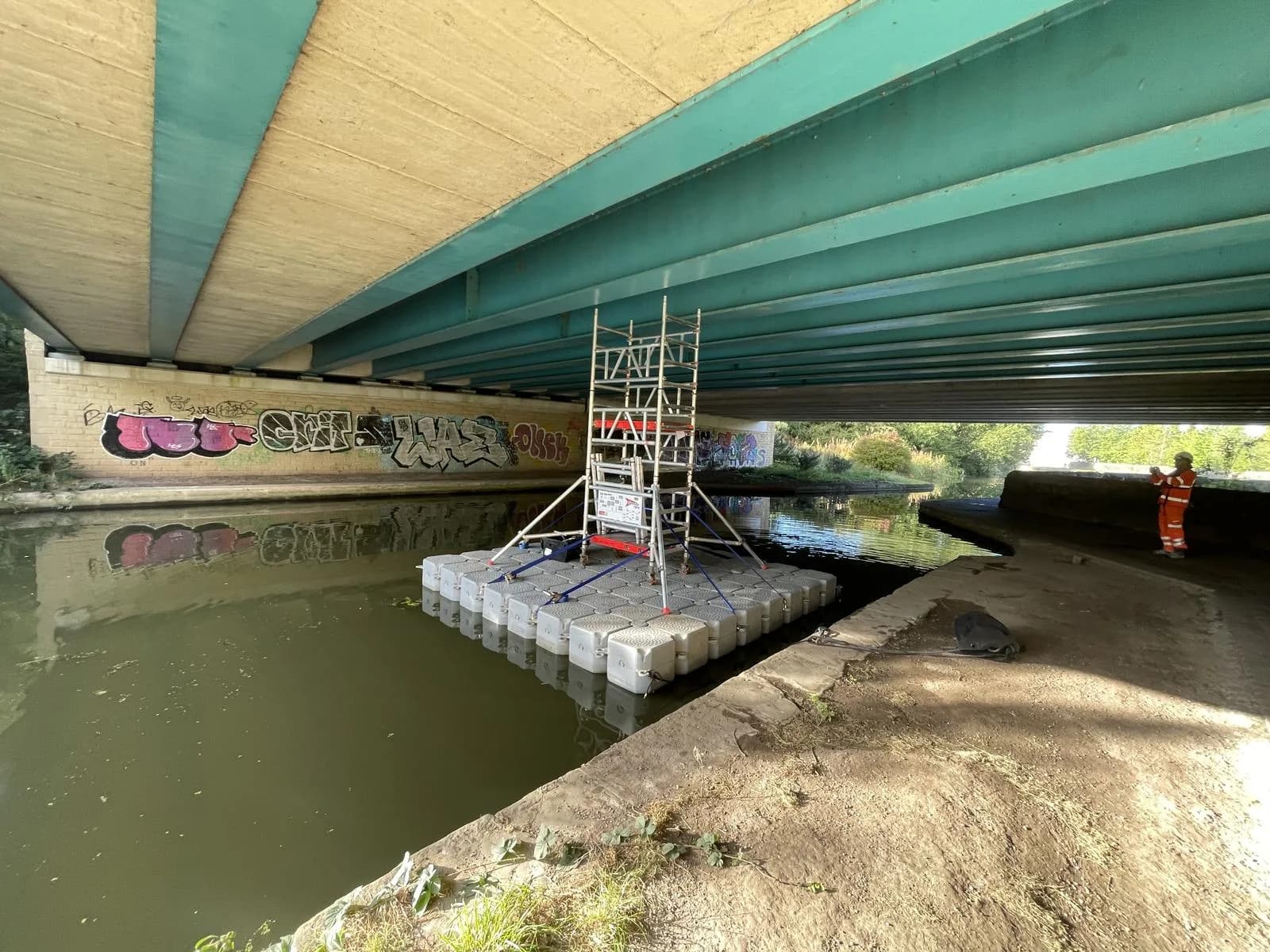 Floating pontoon scaffold tower built on a canal beneath a road bridge